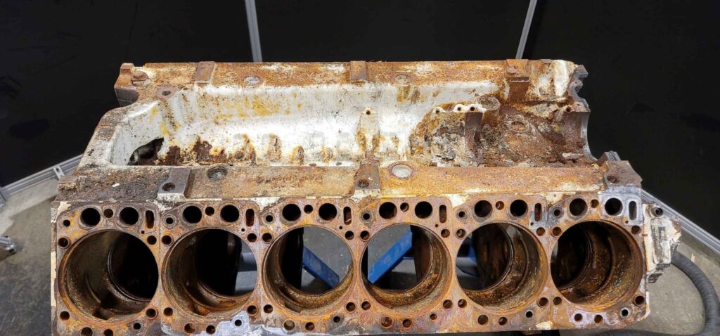 A close-up of a rusty engine block featuring multiple holes, showcasing its weathered and deteriorated condition.
