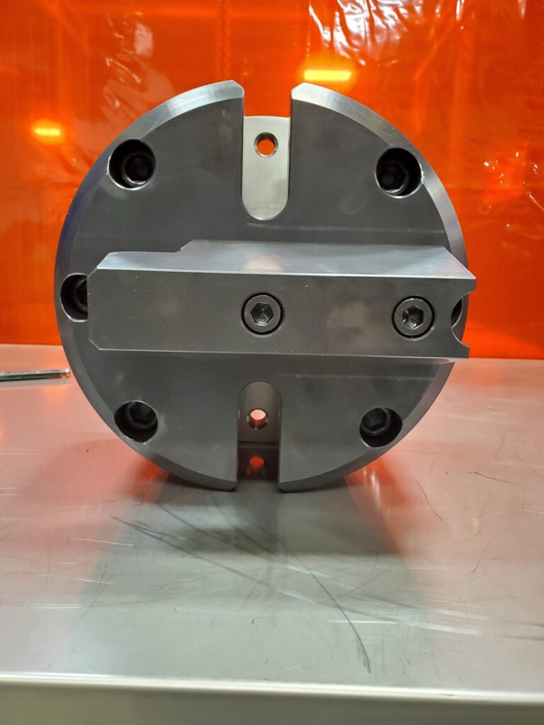A metallic circular component with several holes and bolts, mounted on a flat surface with an orange background.