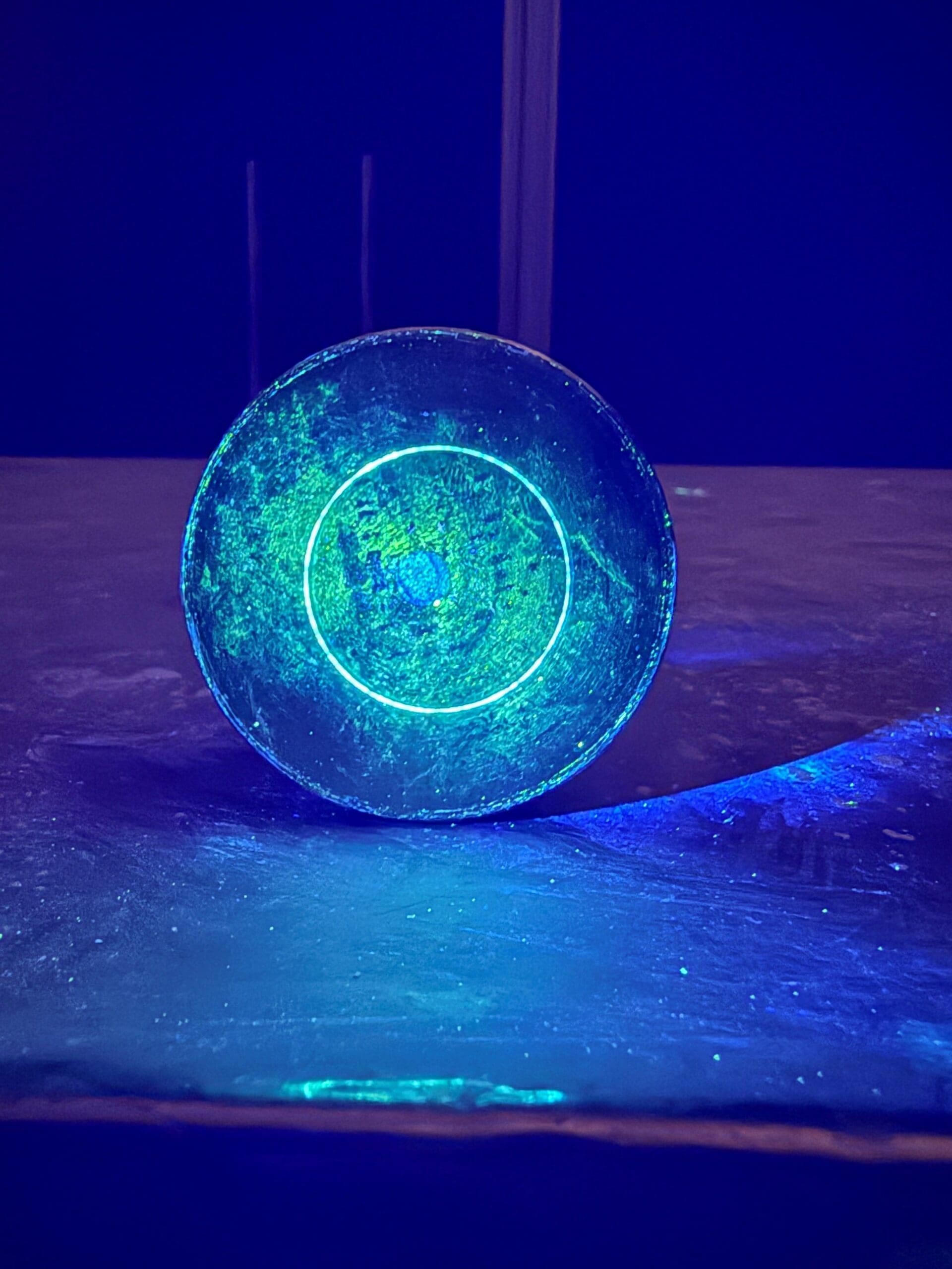 First Development Ring on Bottom is glowing blue as it rests on a table, illuminated by a soft green light surrounding it.