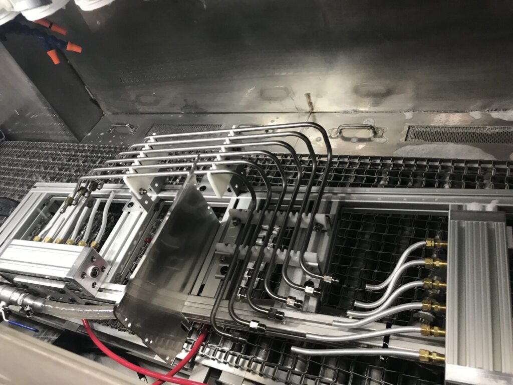 The image shows a complex assembly of metal pipes and components, likely part of an industrial or mechanical system. The setup includes several bent metal tubes connected to various fittings and brackets, mounted on a metallic grid or frame.