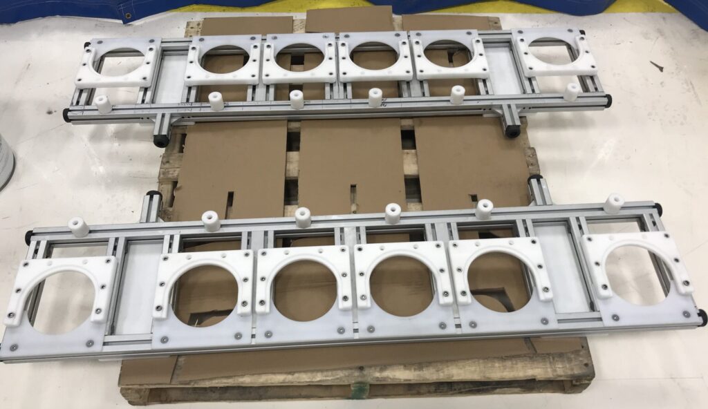 The image shows two identical metal frames with multiple circular cutouts, placed on a wooden pallet. The frames appear to be part of an industrial or mechanical assembly, possibly for holding or aligning components.