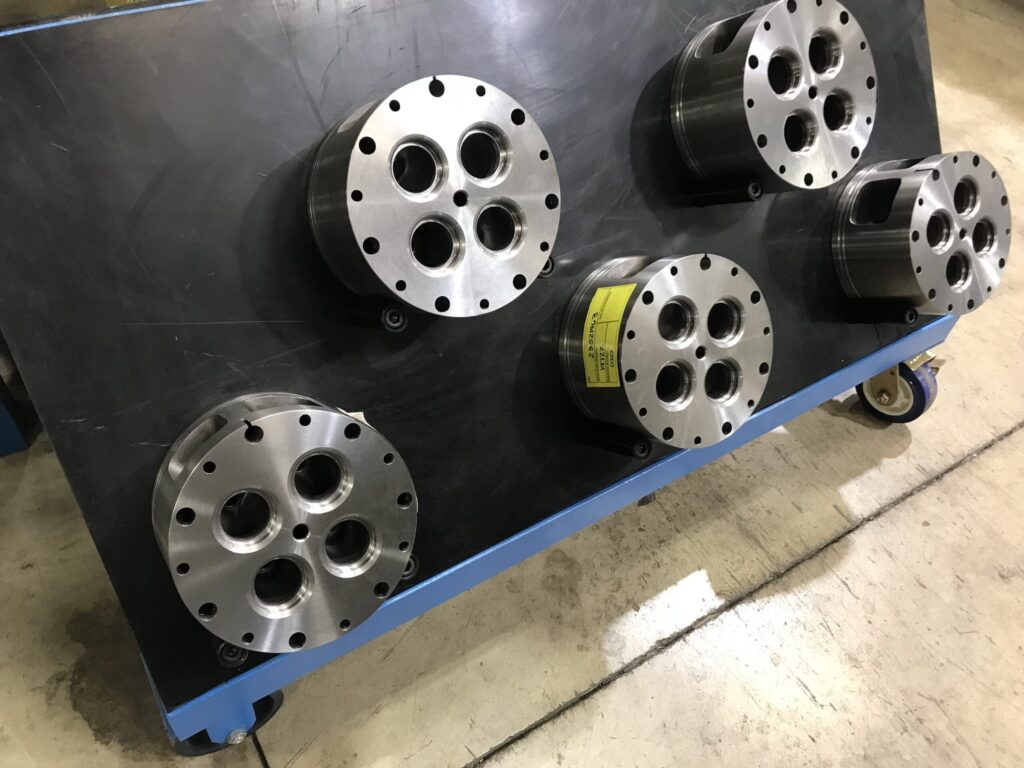 Five metallic cylindrical components with multiple circular holes arranged in a pattern, placed on a black cart with blue edges.