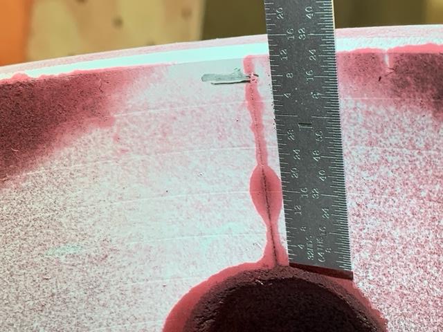 Close-up of a blood red stain with a ruler beside it, emphasizing the contrast between the vase's color and the ruler's linear design.