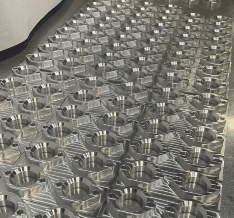 The image shows a large number of identical metallic components arranged in a grid pattern. Each component appears to be cylindrical with a central hole and is placed on a flat surface. The components have a shiny, reflective finish, indicating they are likely made of metal.