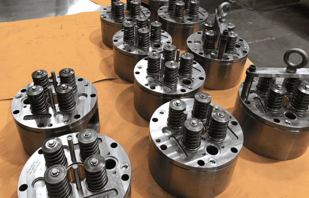 The image shows several cylindrical metal components with multiple springs and bolts arranged on a flat surface. These components appear to be mechanical parts, possibly related to engines or machinery.